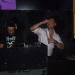 DJ Gilano hinter einem DJ-Pult, daneben ein tanzender Mann