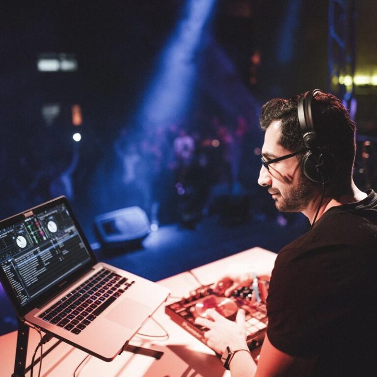 DJ Equipment mit DJ der Kopfhörer aufhat, im Hintergrund dunkel mit Lichteffekten.