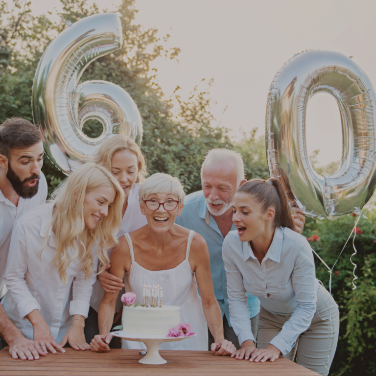 Fünf Personen stehen um eine alte Dame vor einer weißen Geburtstagstorte, im Hintergrund zwei silberne Ballons mit der Zahl 6 und 0